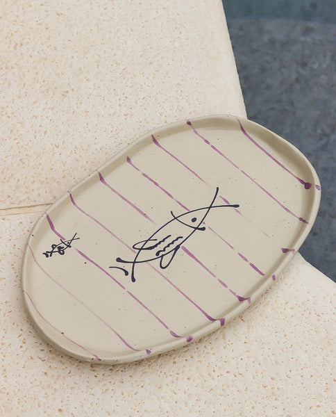 Oval ceramic plate with purple stripes and fish design on a textured surface