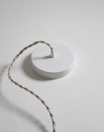 Suspension dôme arrondi blanche avec cordon torsadé beige posé sur une surface claire.