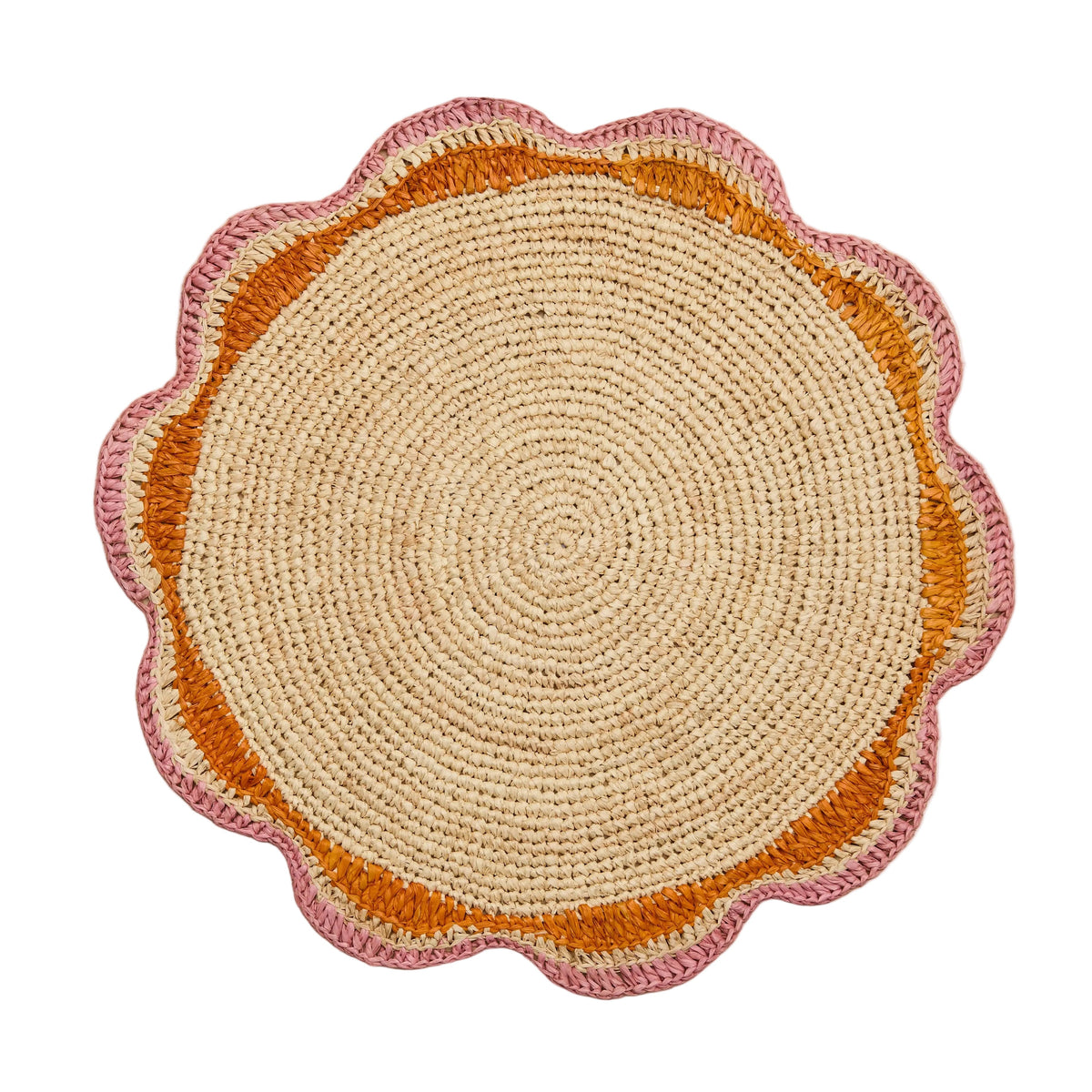 A round pink woven placemat with a scalloped edge design, placed on a wooden surface.