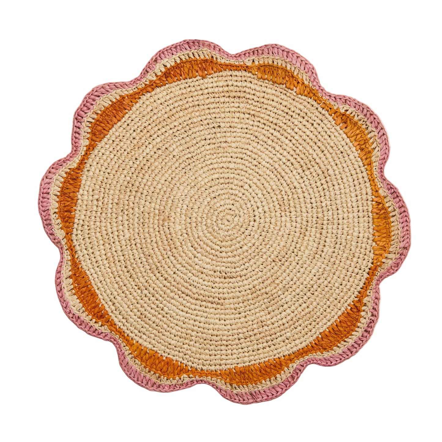 A round pink woven placemat with a scalloped edge design, placed on a wooden surface.