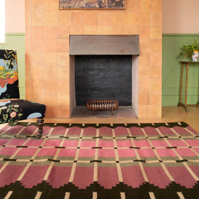 Pink and green geometric flatweave wool rug in a colourful room.