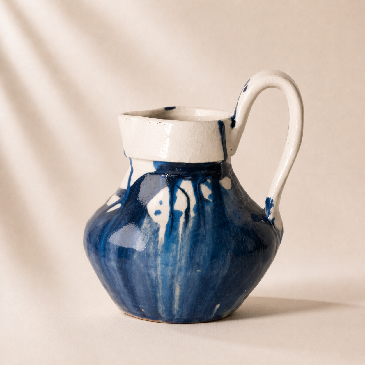 Ceramic pitcher with blue and white abstract design on a beige background