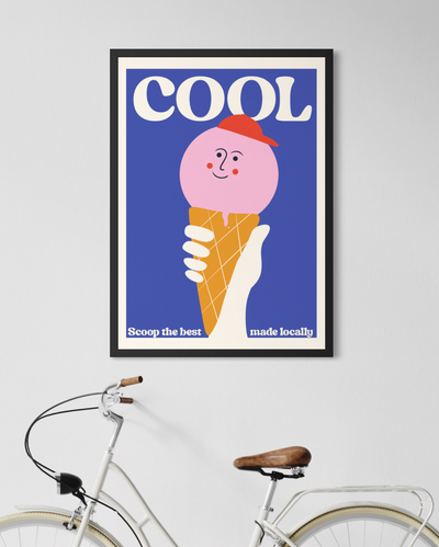 A framed art print featuring a retro-style illustration of a pink ice cream scoop on a cone against a blue background, with the word 'COOL' at the top. Coastal print, British seaside decor. 