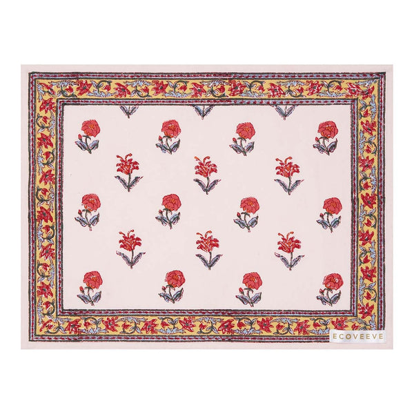 A hand-block printed cotton table mat with a floral pattern in red and yellow on a white background, bordered with a blue and orange design.