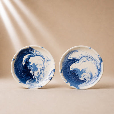Two ceramic plates with blue and white marbled design on a beige background