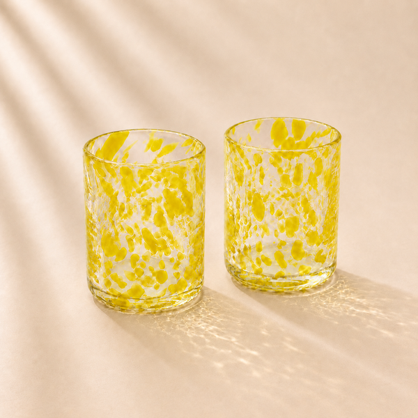 Two yellow and white marbled glass tumblers on a beige background