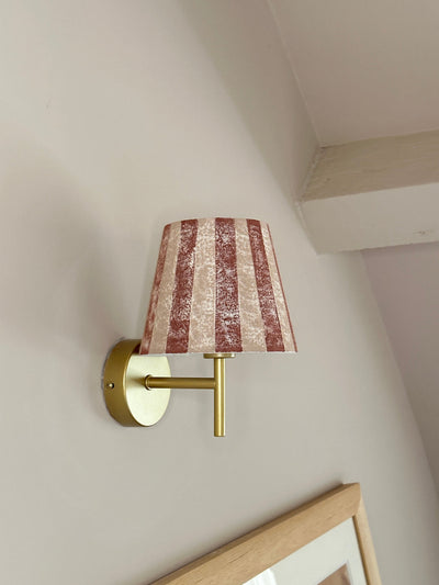 Bold stripe lampshade in burgundy and pink, styled as a wall light shade on a brass sconce. A striped lampshade design perfect for striped lighting and empire light shades in UK interiors.