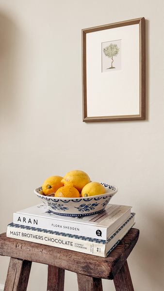 Bowl of lemons on books with a framed picture of a Lemon Tree the wall