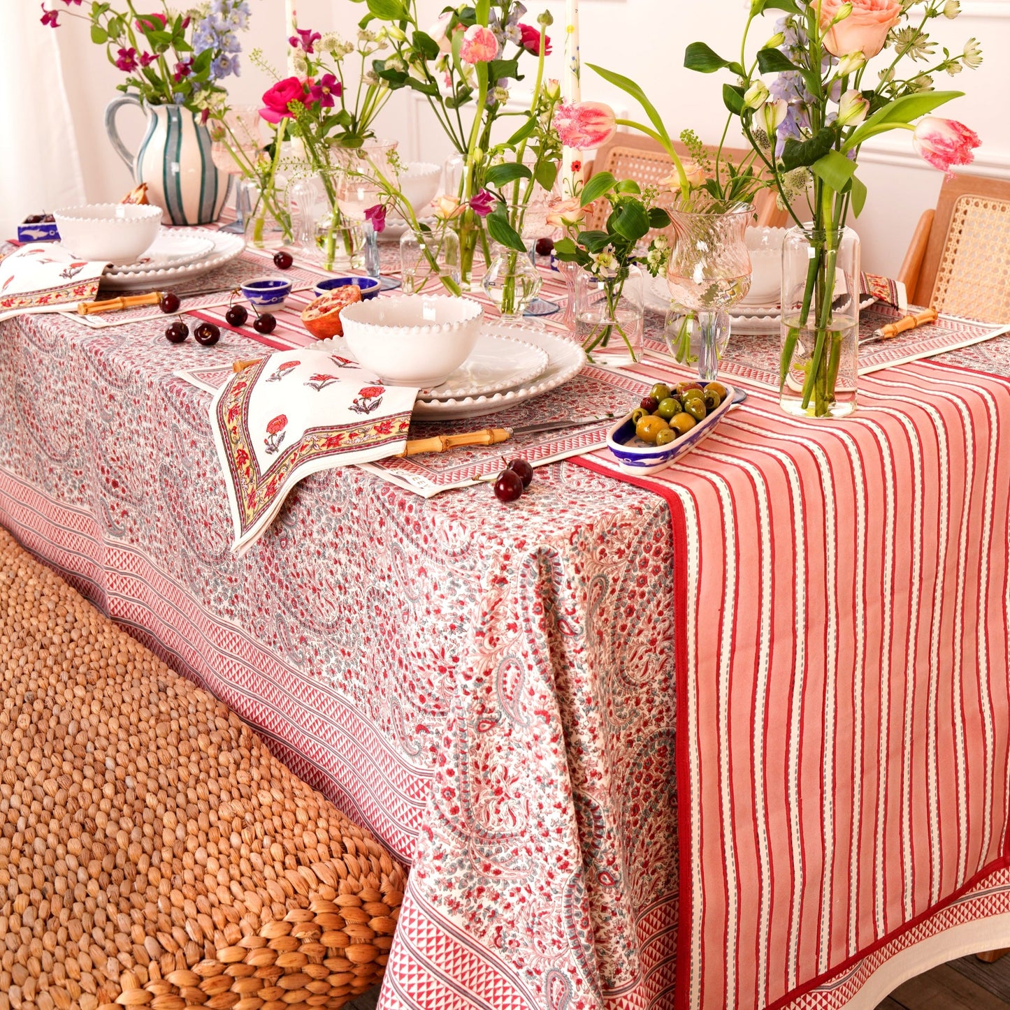 Dining table with a block printed red and white patterned tablecloth, runner, table linens, flowers, and decorative items.