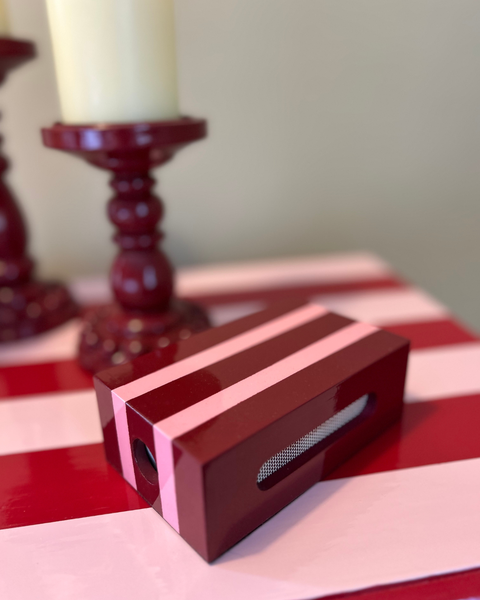 Hand-painted red and pink striped matchbox case styled beside a candle on a decorative tray with colourful home accessories.