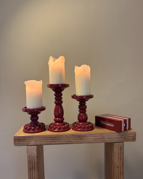 Hand-painted bobbin candle holders styled with pillar candles with matchbox case and lit candles on wooden bench