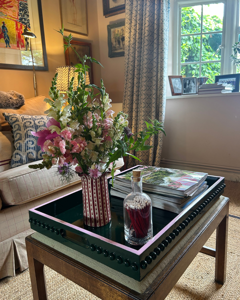 Decorative tray with flowers and a bottle on a coffee table in a living room.