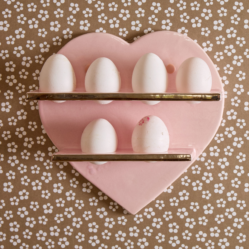 Heart-shaped pink egg holder with six white eggs on a patterned background.