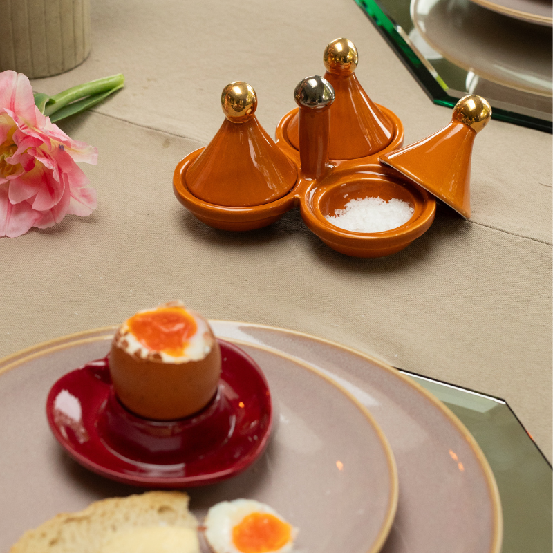 Set of ceramic tagines for salt, pepper and spice storage with an egg cup holding a dippy egg on a plate in the foreground.