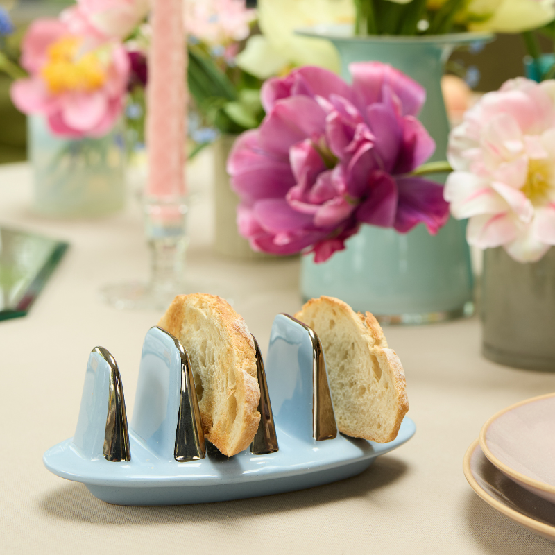 Blue toast rack with rustic white bread slices on a breakfast table with flowers in the background.