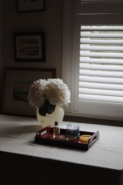 Vinidec small dual-tone lacquered tray in cherry red and sand styled on table with candle perfume and white hydrangeas