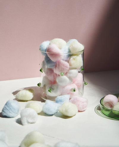 The OCTAEVO Agave Glass Container Small, filled with pastel cotton balls, sits beside a green dish and scattered balls.