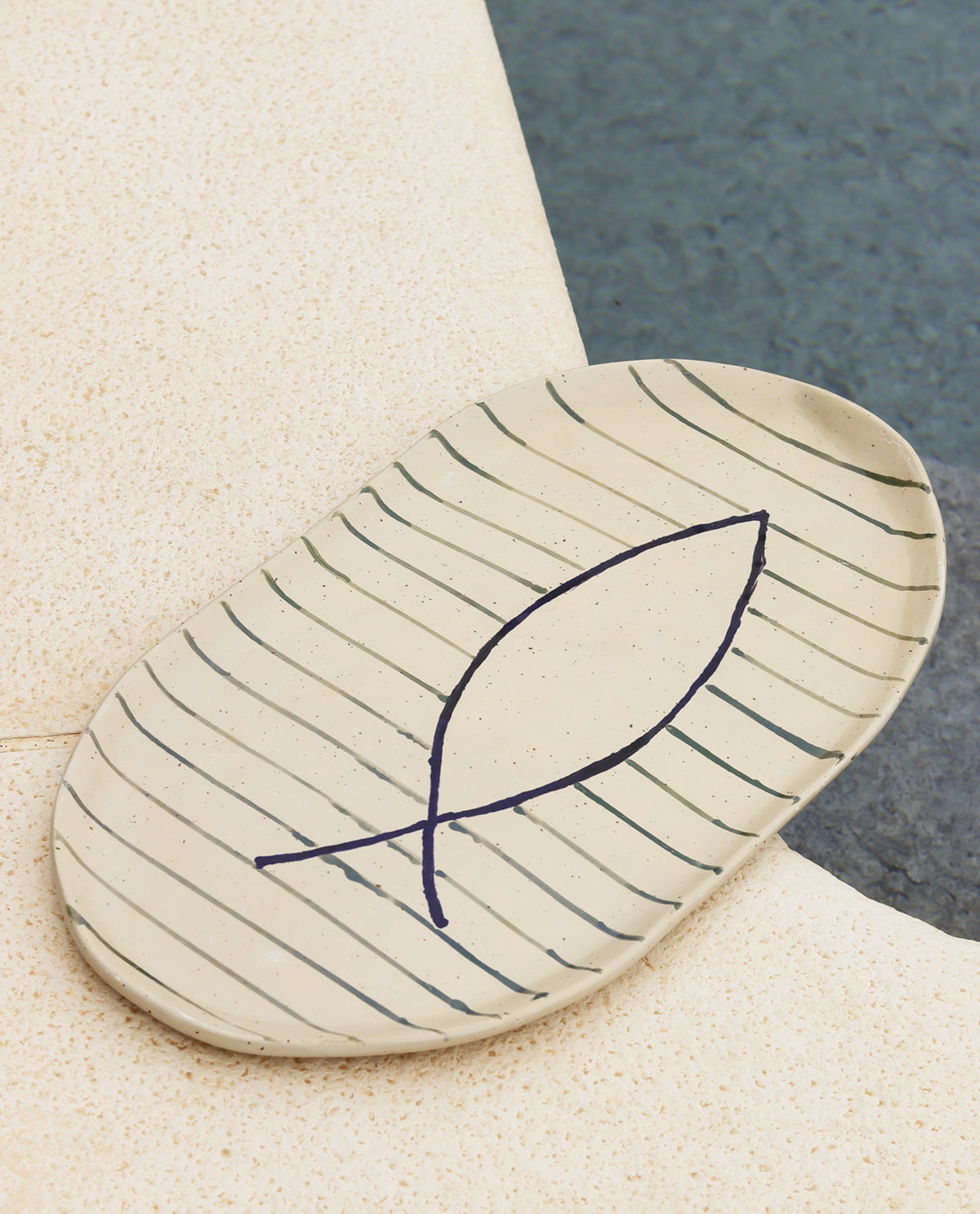A beige oval ceramic serving platter with a striped pattern and a single fish illustration in the center.