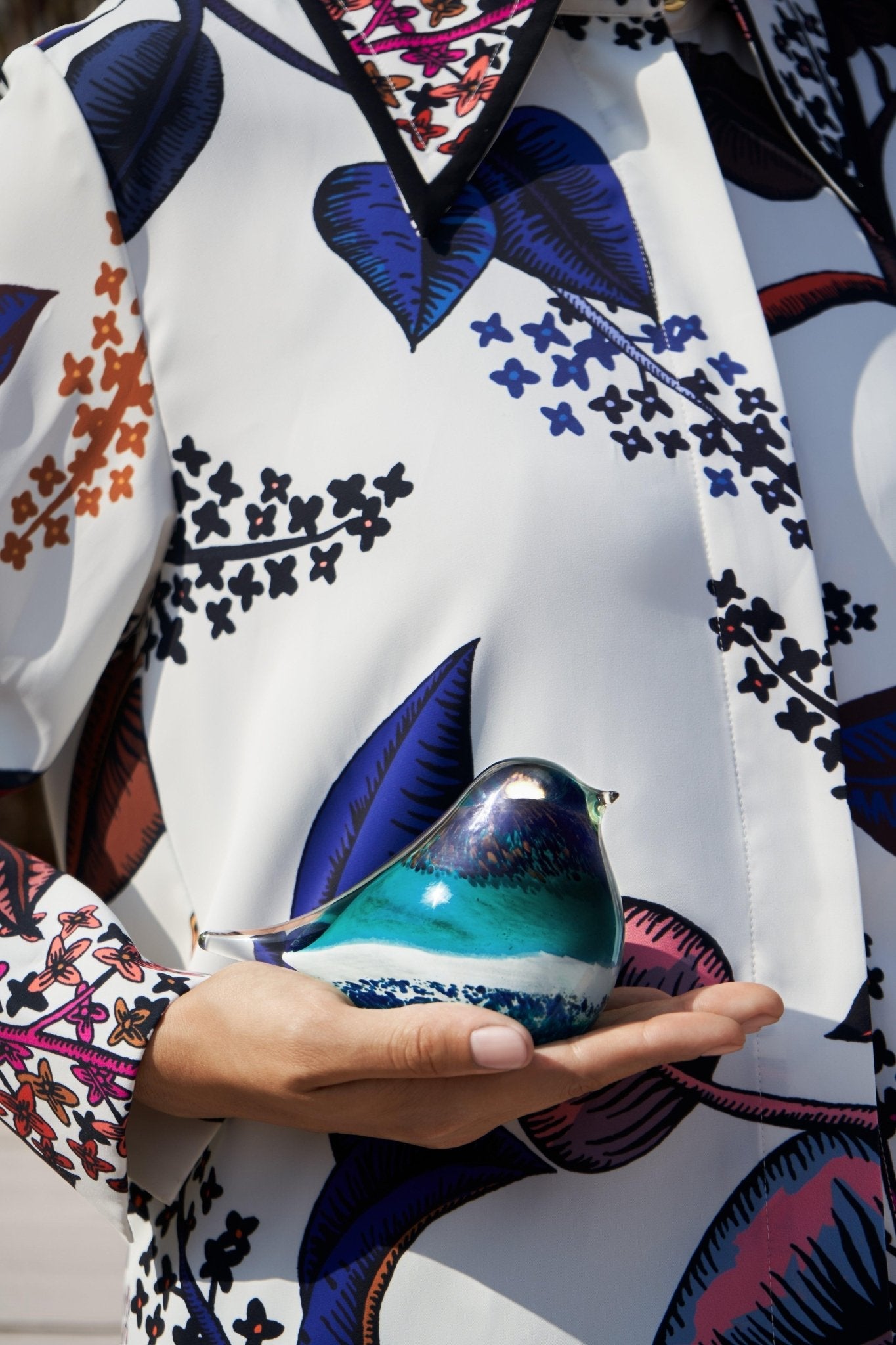 A person in a floral shirt holds the green OCTAEVO Atlas Glass Bird. 