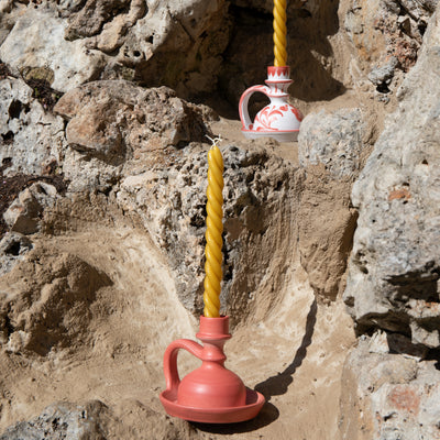 Pink and white ceramic vessels with yellow candles against a rocky background -lifestyle