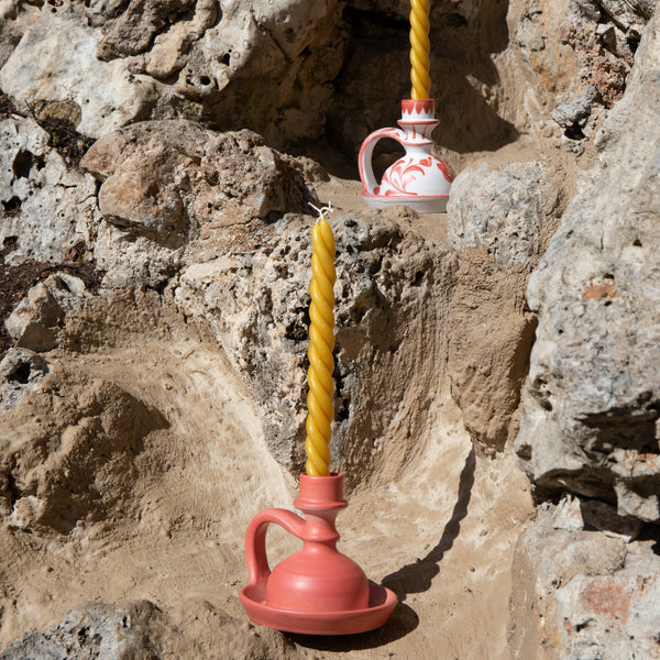 Pink and white ceramic vessels with yellow candles against a rocky background -lifestyle