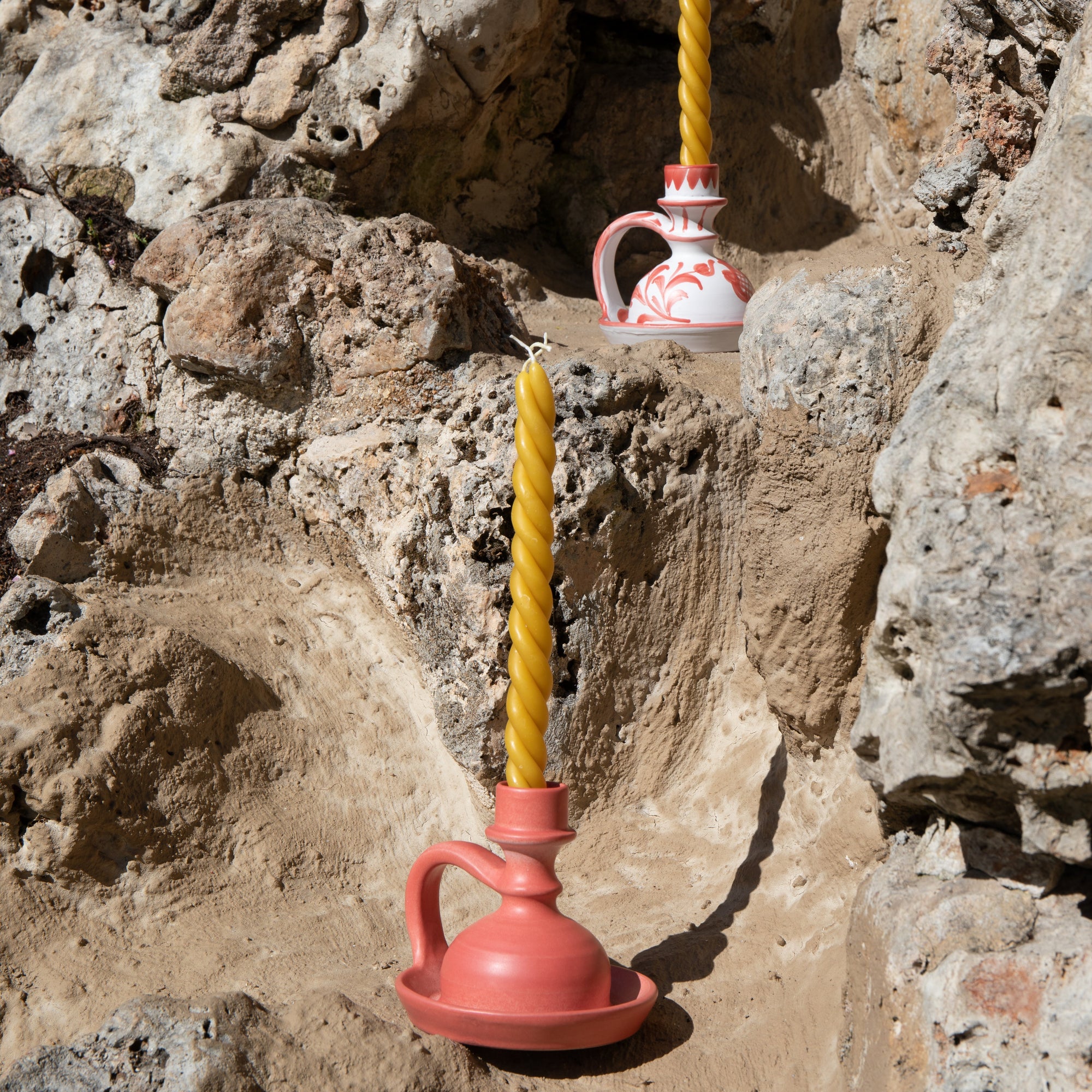 Pink and white ceramic vessels with yellow candles against a rocky background -lifestyle