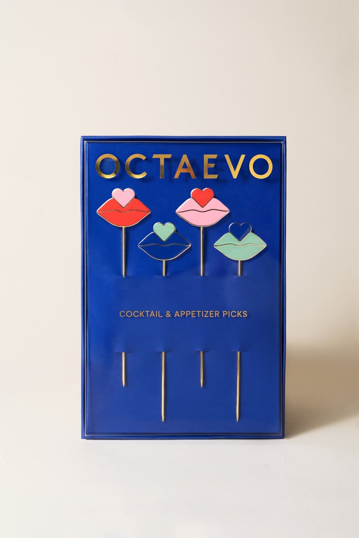 The OCTAEVO Beso Cocktail Picks set includes four gold-plated picks shaped like lips and a heart in a blue box.