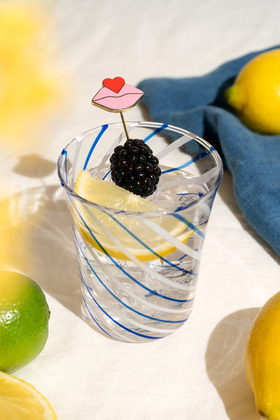 A glass of sparkling water garnished with OCTAEVO Beso Cocktail Picks (Set of 4) and fresh fruit.
