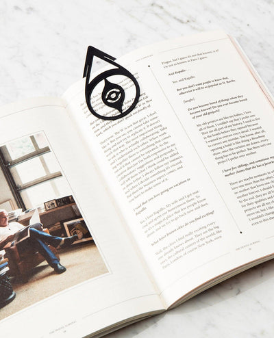 OCTAEVO’s Bookmark Nazar, a black brass charm for luck, rests on an open book. 