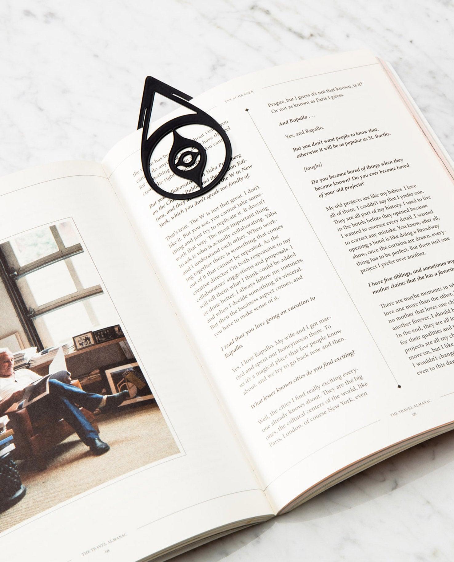 OCTAEVO’s Bookmark Nazar, a black brass charm for luck, rests on an open book. 
