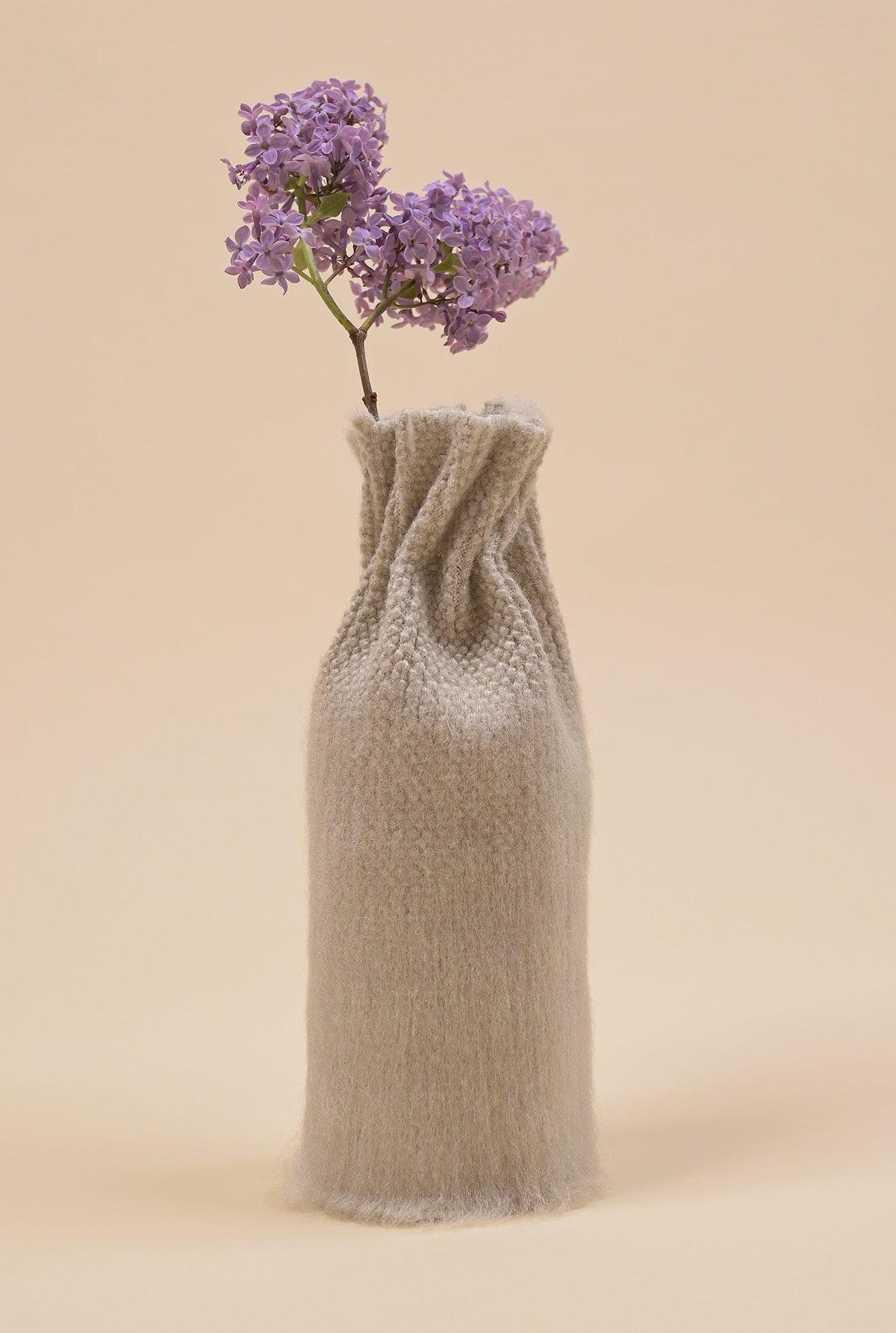 side view of beige knit textile vase in brushed silk and organic cotton with flower and beige background
