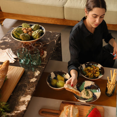 Woman sitting at a table with food and a dog in a cozy living room.