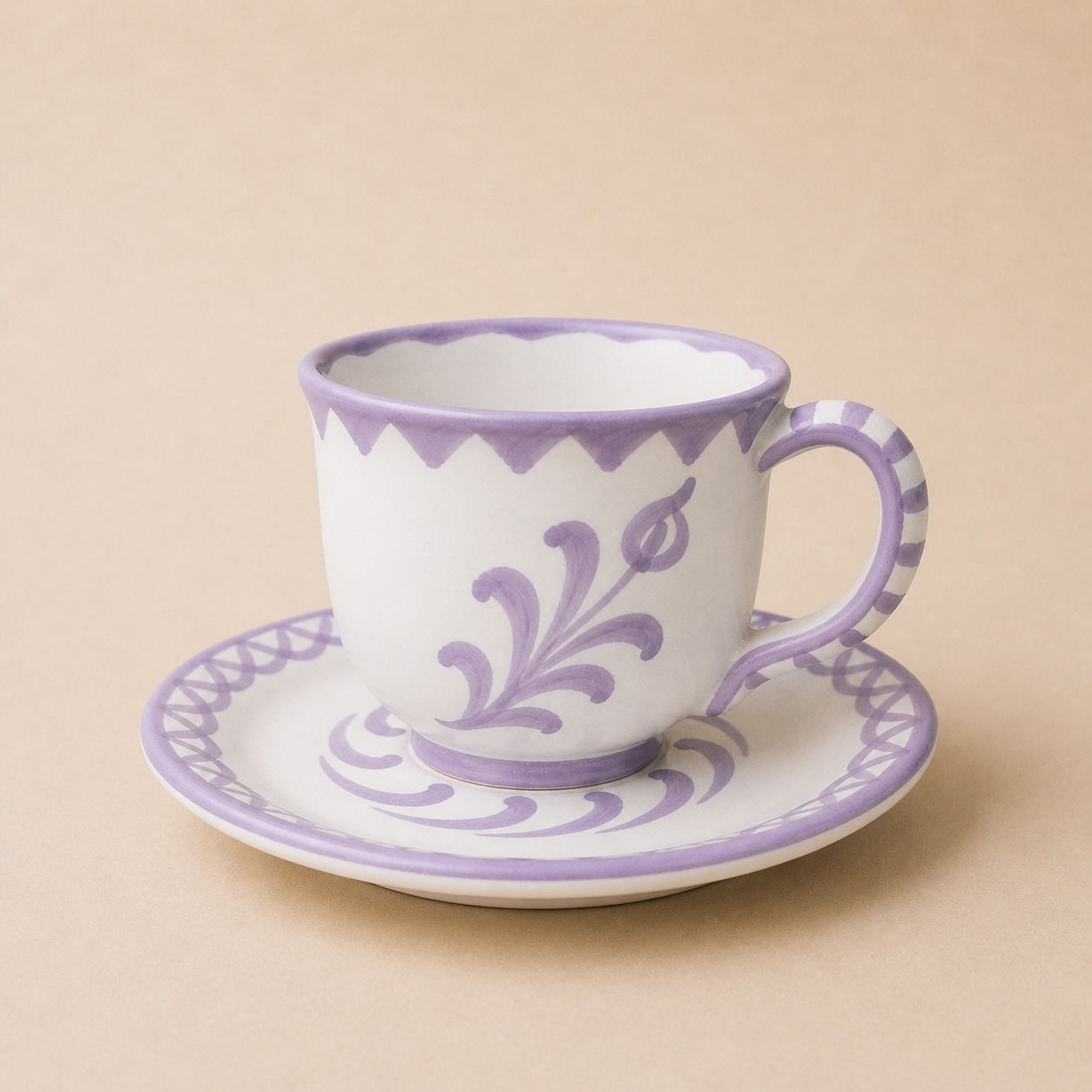 Ceramic cup and saucer with purple floral patterns on a beige background