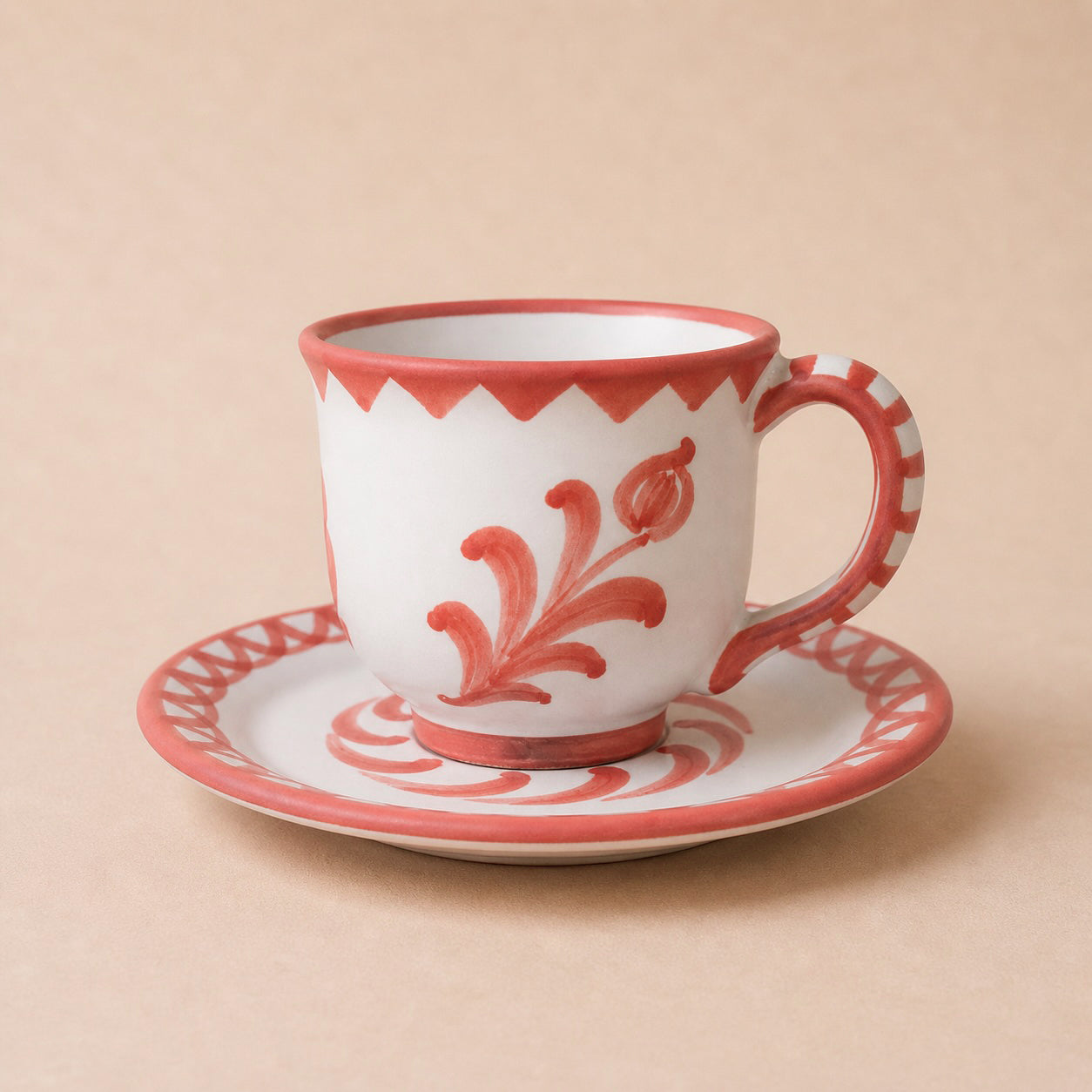 Ceramic cup and saucer with red floral patterns on a beige background