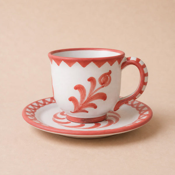Ceramic cup and saucer with red floral patterns on a beige background