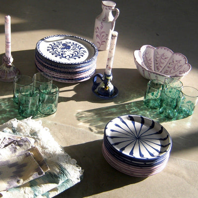 Ceramic plates with blue patterns on a table with green glasses and decorative items. - lifestyle