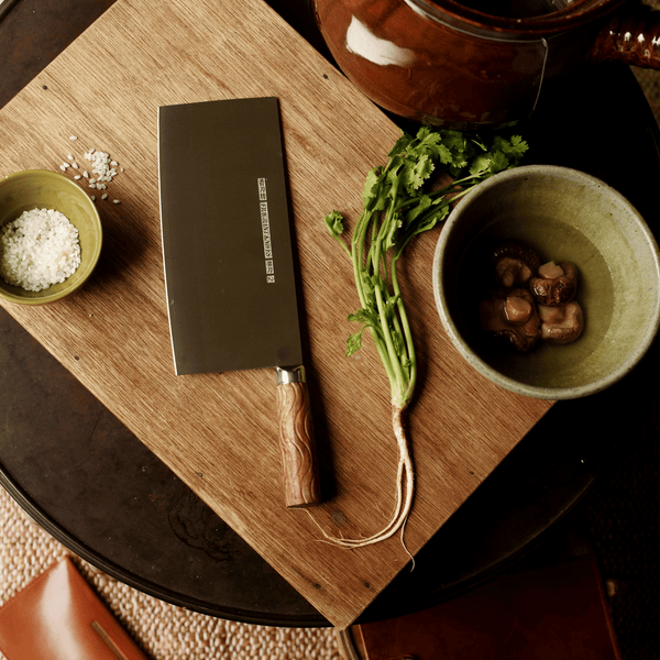 High-carbon steel knife on a wooden cutting board with bowls of Chinese ingredients