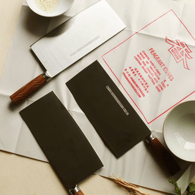 Two cleavers with rosewood handles on a surface with a 'Fragrant Knives' traditional branded Chinese knife paper.