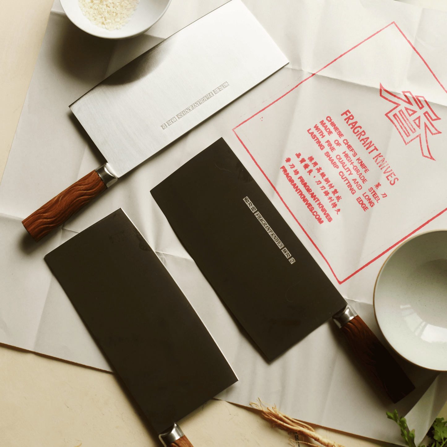 Two cleavers with rosewood handles on a surface with a 'Fragrant Knives' traditional branded Chinese knife paper.