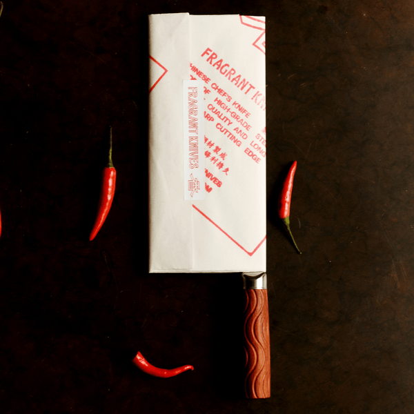 Knife with wooden handle on a dark surface, surrounded by red chilies.