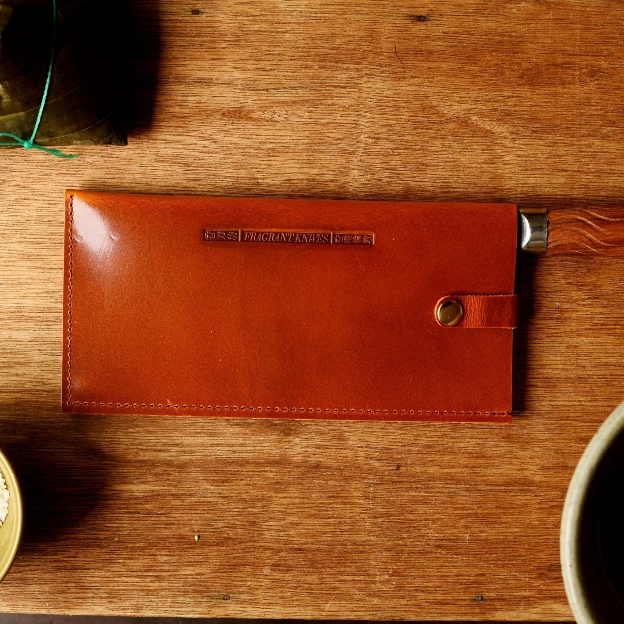 Brown leather knife sheath on a wooden surface with bowls of ingredients.