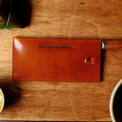Brown leather knife sheath on a wooden surface with bowls of ingredients.