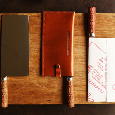 Three knives with sheaths on a wooden cutting board