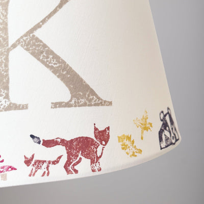 Close-up of a personalised kids lampshade with woodland animals design, featuring a fox and the letter K. Handmade empire lampshade ideal for kids bedroom decor, animal lampshade for boys lampshade or girls lighting. Perfect as a personalised kids gift, personalised christening present, or new parent gift.