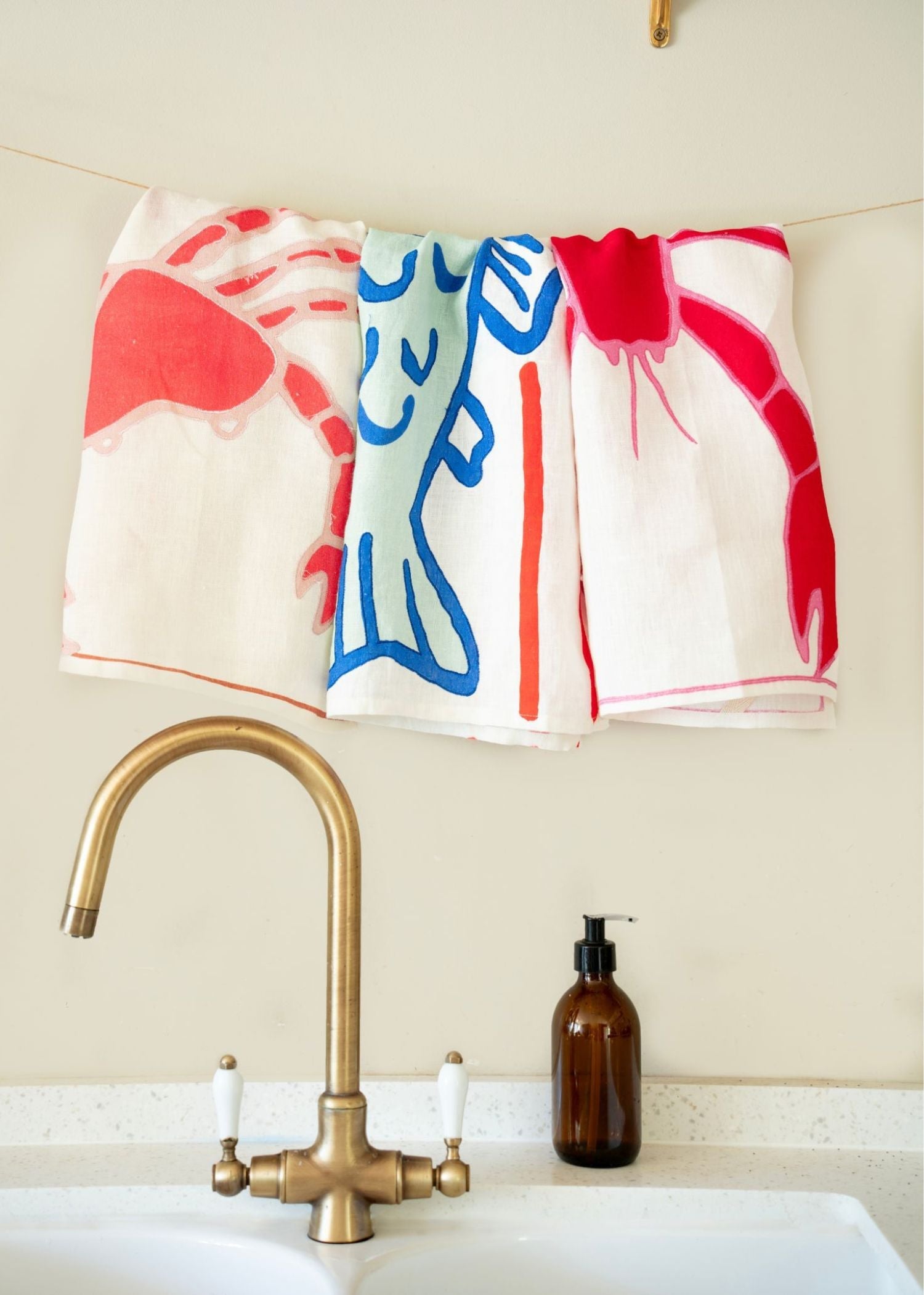 Set of 3 coastal-inspired tea towels hanging above a sink by Amuse La Bouche