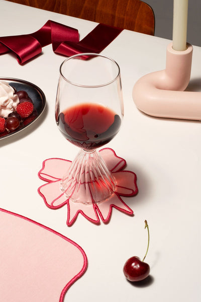A glass of red wine on an Octaevo Coquette Coaster beside a cherry and fruit plate on a white table.