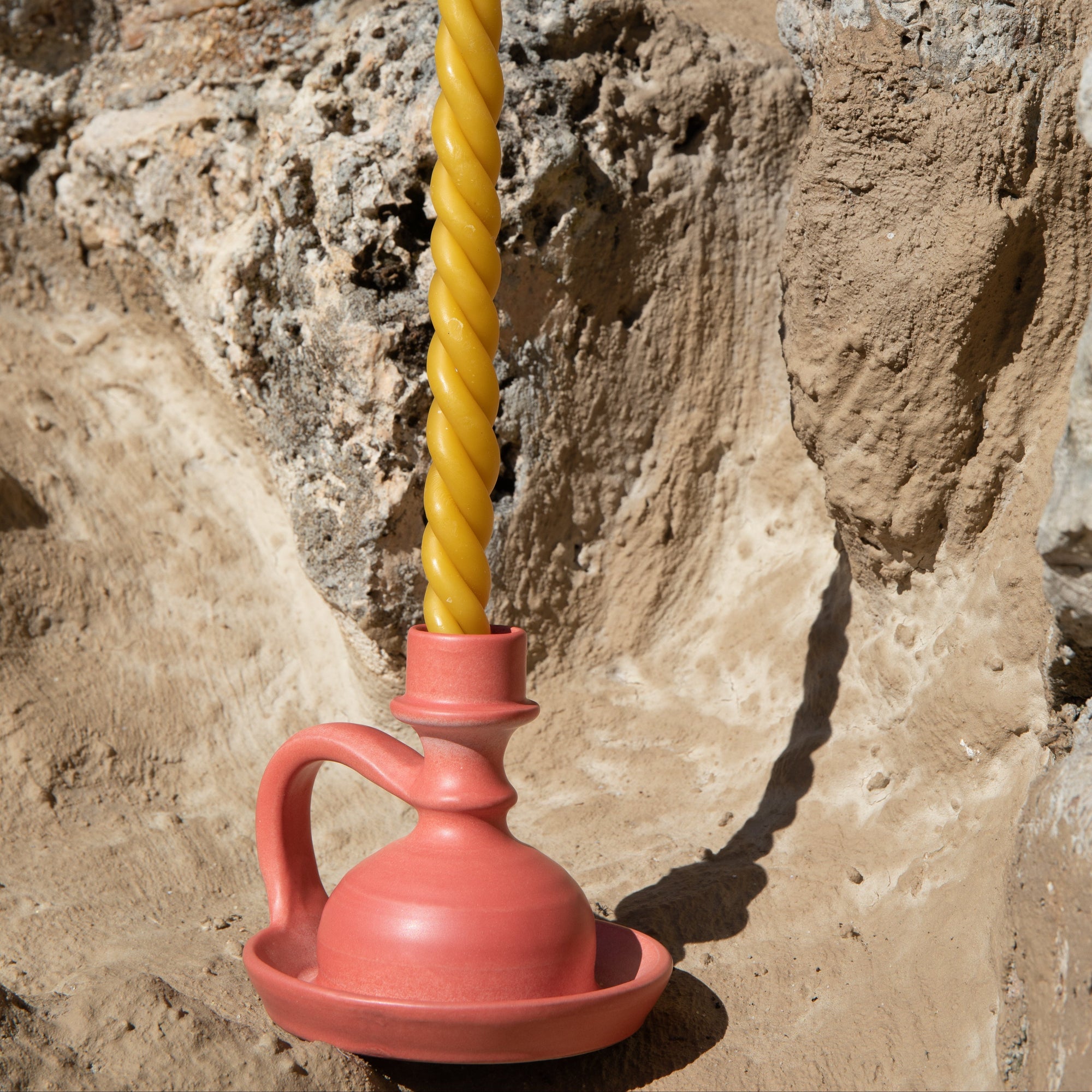 Yellow twisted candle in a red ceramic holder against a stone wall. - lifestyle