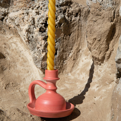Yellow twisted candle in a red ceramic holder against a stone wall. - lifestyle