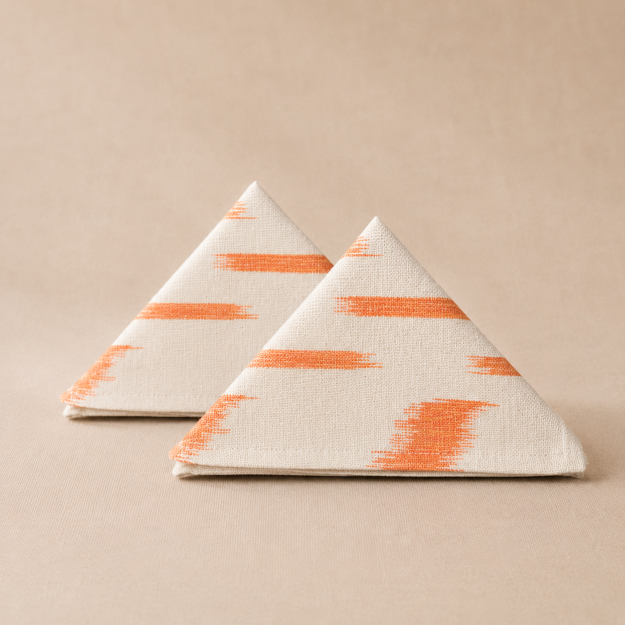 Two triangular napkins with orange pattern on a beige background