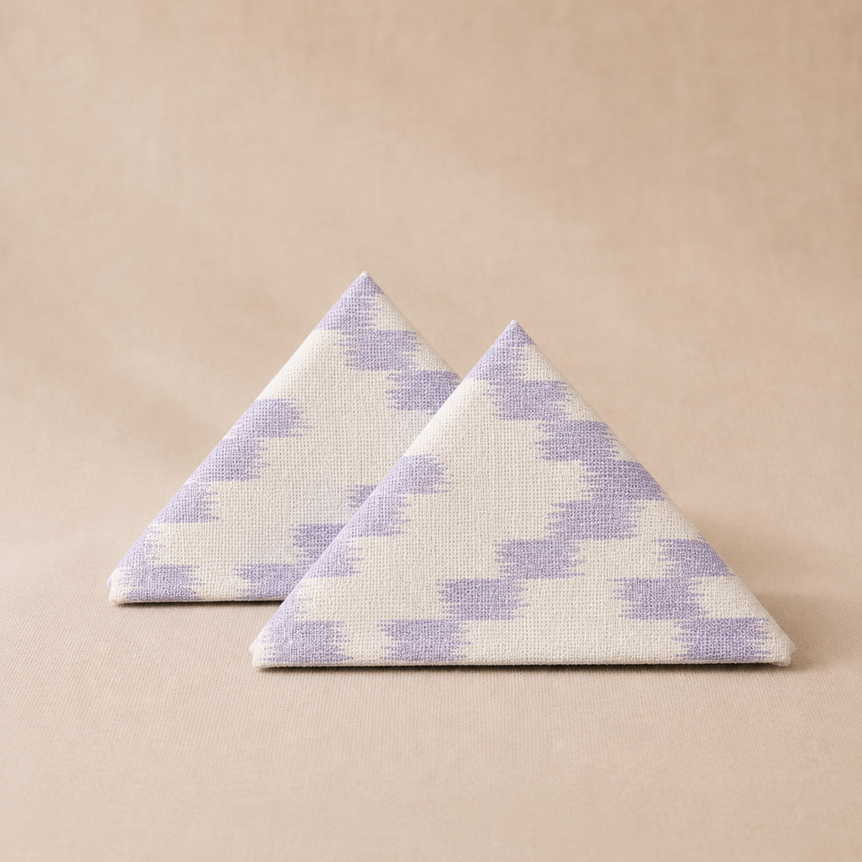 Two triangular napkins with a purple and white pattern on a beige background